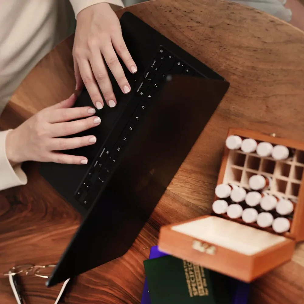 Mâini scriind la laptop, lângă o trusă cu remedii homeopate